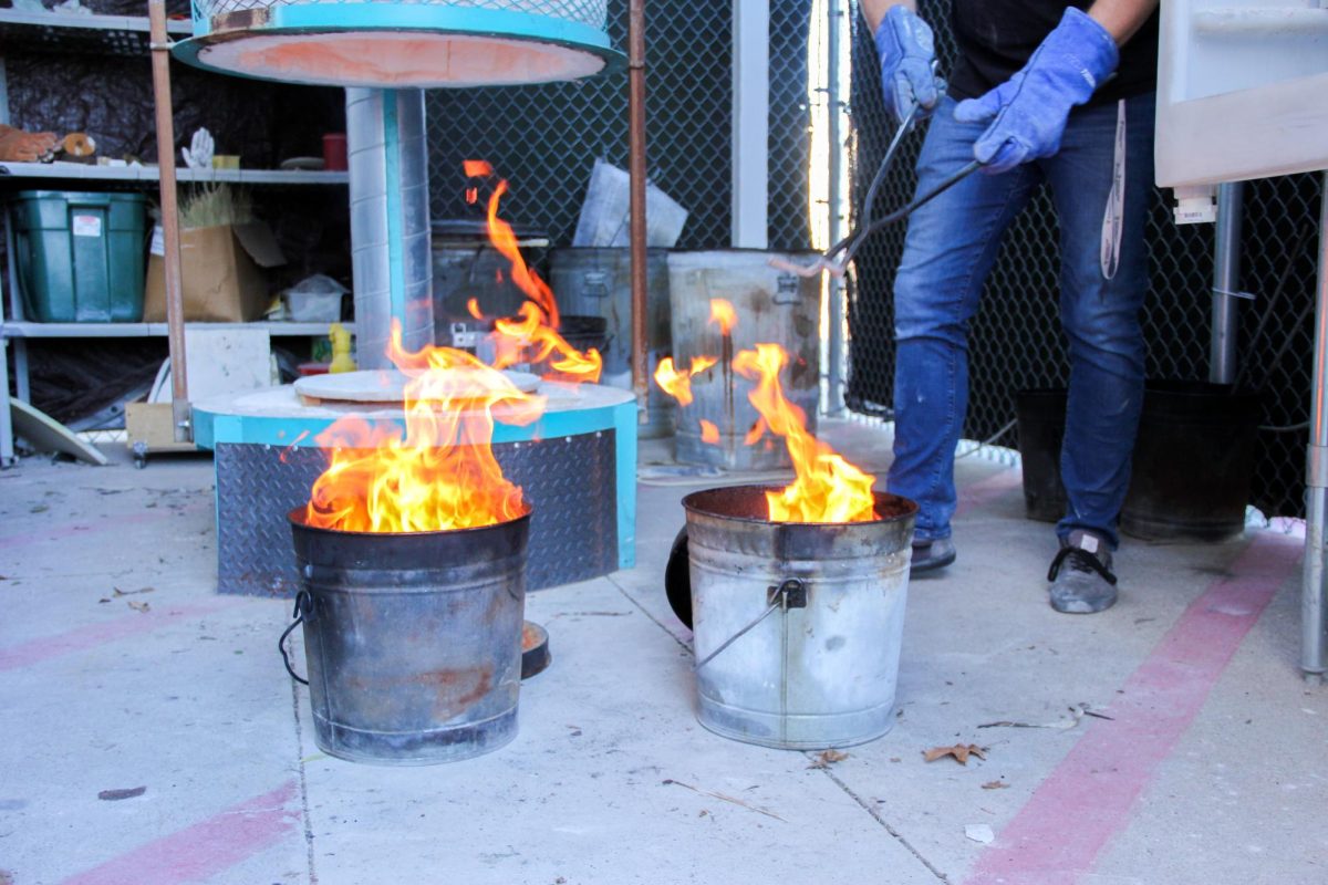 NW Clay Club sponsor Jacob Steed places raku fired pieces in the fire buckets to create a specialized glaze effect.