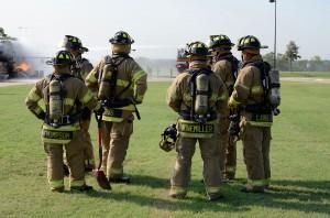 Participants in the aircraft mishap exercise discuss their plan on how to extinguish the fire as another group of firefighters puts out the flames.