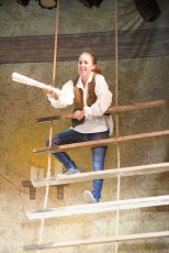 Cast member Katie de Groh rehearses a narration while hanging off of a ladder in Treasure Island.