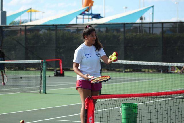 NE+student+Ingrid+Pineda+serves+tennis+balls+for+children+to+practice+their+backhand+swing.