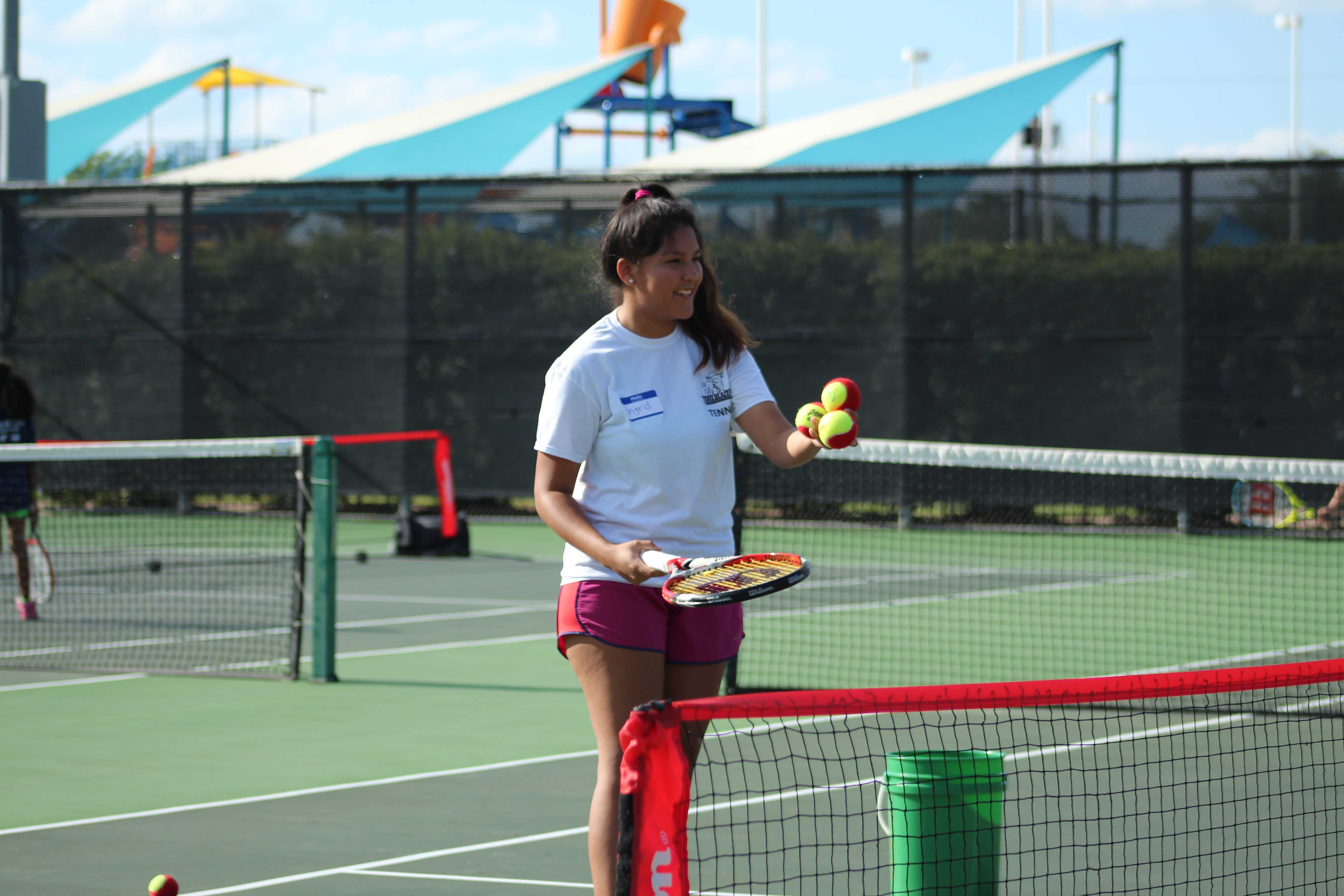 NE student Ingrid Pineda serves tennis balls for children to practice their backhand swing.