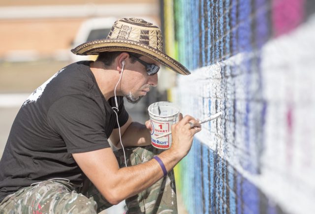 Vallarino uses a white exterior paint to complete the border on the mural he is working on outside of the Community Market in Burleson.