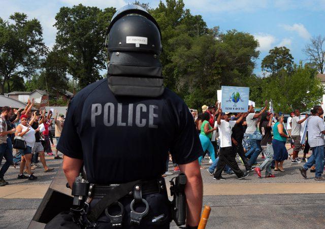 A+police+officer+watches+as+protesters+march+in+front+of+the+Ferguson%2C+Missouri%2C+police+station+in+August+2014.+Law+enforcement%E2%80%99s+treatment+of+minorities+has+continued+to+be+a+nationwide+issue+ever+since.