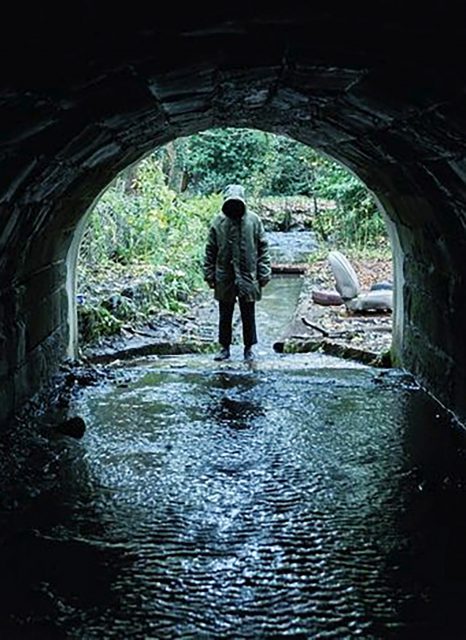 A mysterious figure eerily stands at the end of a tunnel, which is one of many creepy, atmospheric moments in the British horror film Ghost Stories.