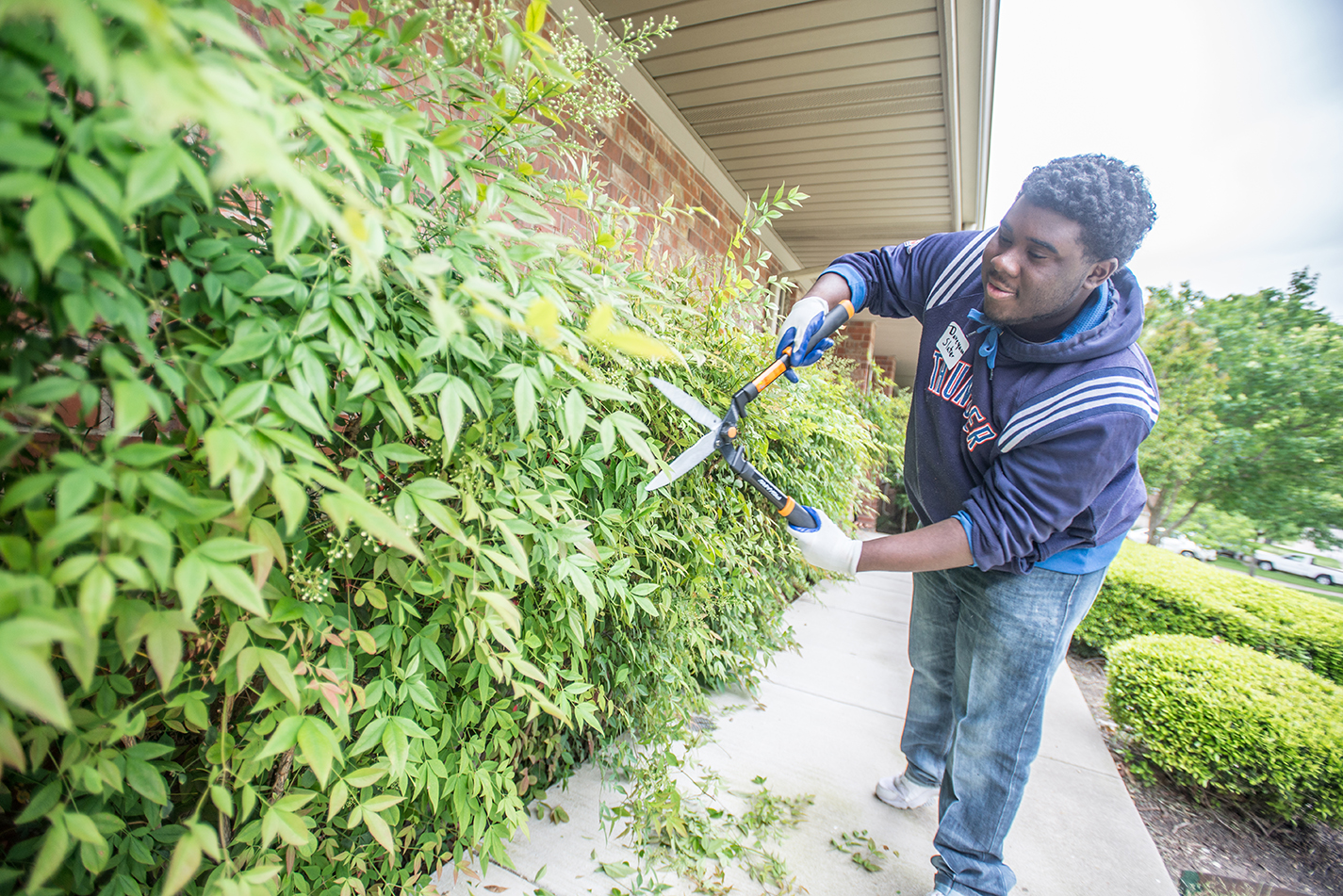 TR student Daveyaun Slater trims hedges at an ACH services home in south Fort Worth. The “Pretty” Park Pavilion group cleaned up yards, a playground and a home.