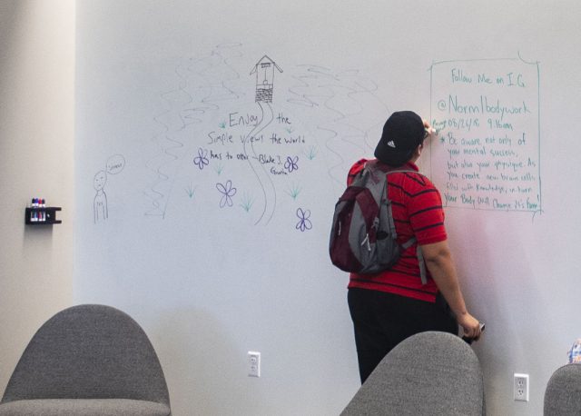SE student Sam Carrillo writes on a dry erase wall in the learning commons.