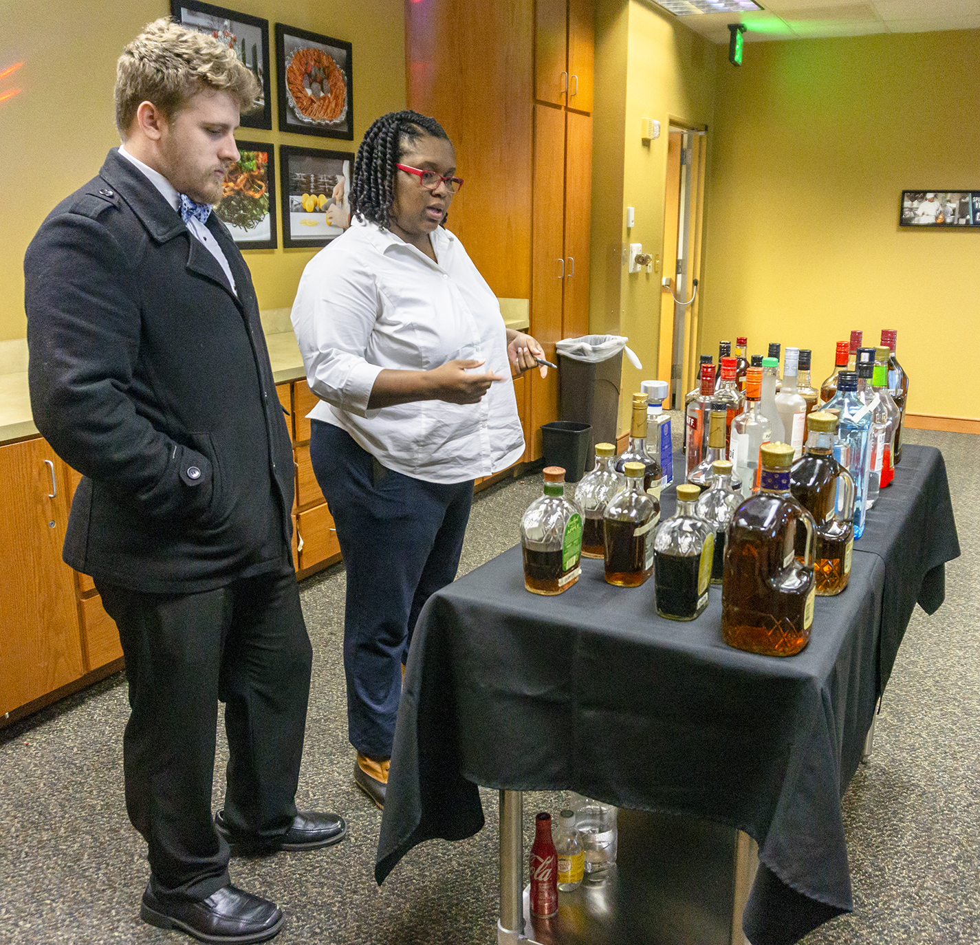 NE and SE student Sam Bailey and SE student Kemy Acosta peruse liquor bottles filled with colored water to inspire them for an assignment to create a unique concoction.