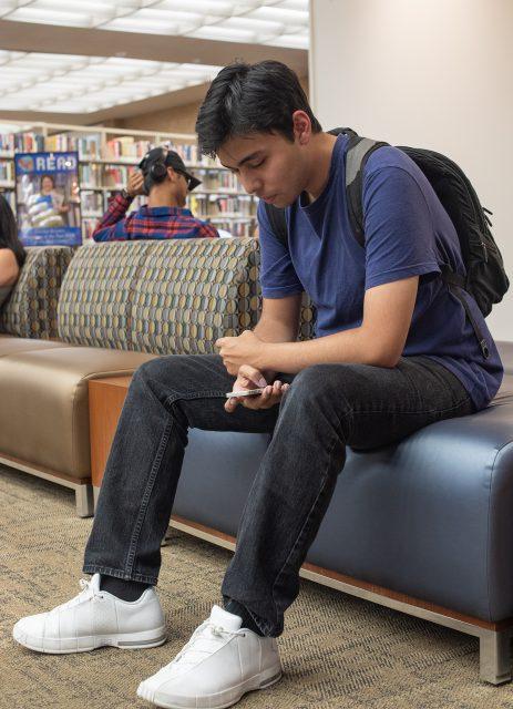NE student Trini Lucio uses his phone while he sits in the library and waits for this next class to start.

Joseph Serrata/The Collegian