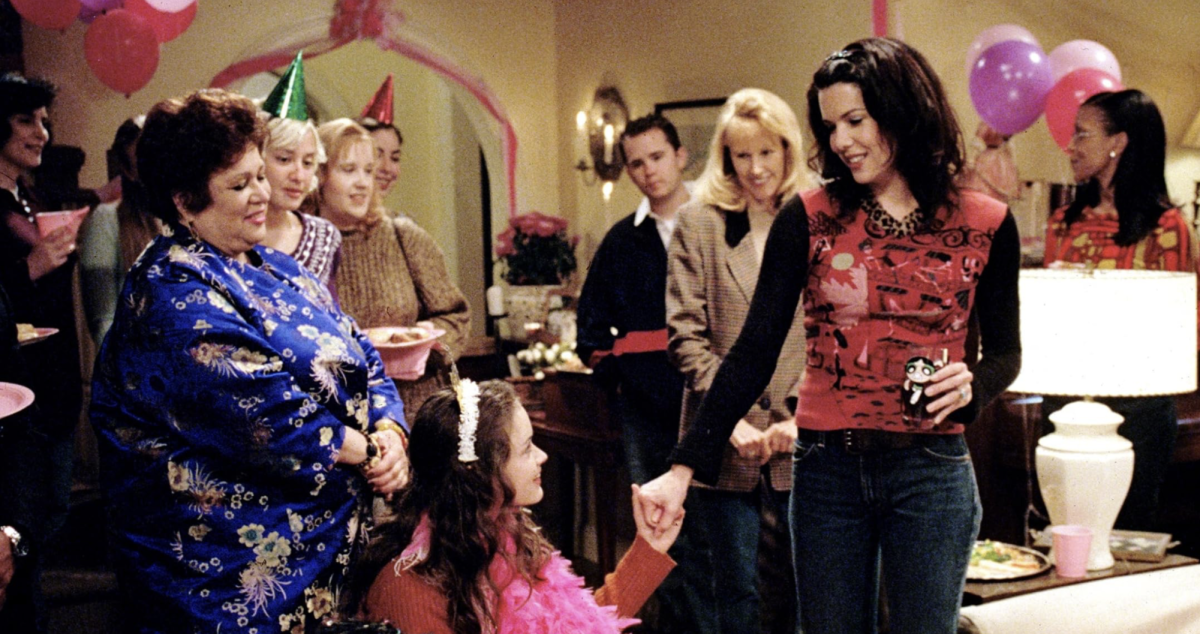 Lorelai Gilmore, played by Lauren Graham, and Rory Gilmore, played by Alexis Bledel, hold hands together while celebrating Rory Gilmore at her birthday party.