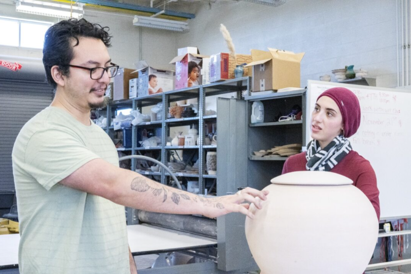 SE ceramics instructor and artist Juan Barroso explains his plan to paint images of immigrant laborers on his handmade vase to lab tech Huda Dorsett.