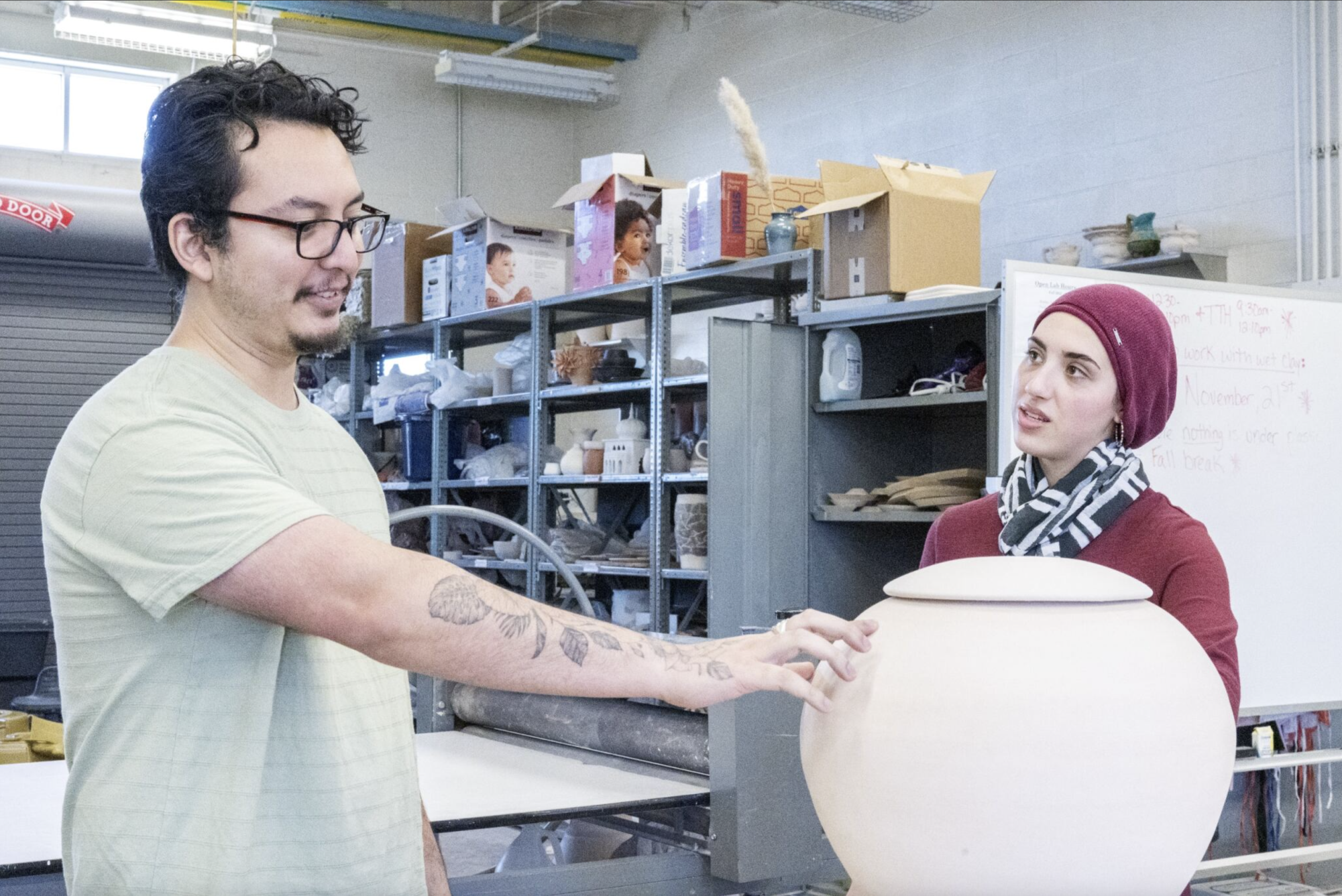SE ceramics instructor and artist Juan Barroso explains his plan to paint images of immigrant laborers on his handmade vase to lab tech Huda Dorsett.