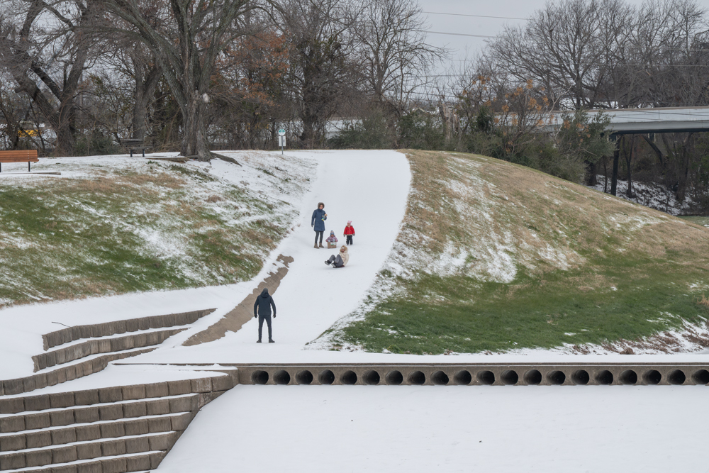 Marina Figurski sleds down a snow-covered sidewalk with her family and friends on Jan. 26 at the Trinity River Trailhead Park in Fort Worth after a massive winter storm hit the DFW metroplex. The Artic winds brought a total of two-and-a-half inches of snow and sleet  Fort Worth, according to WFAA, which resulted in the closure of all TCC campuses Jan. 26, 27 and 28.