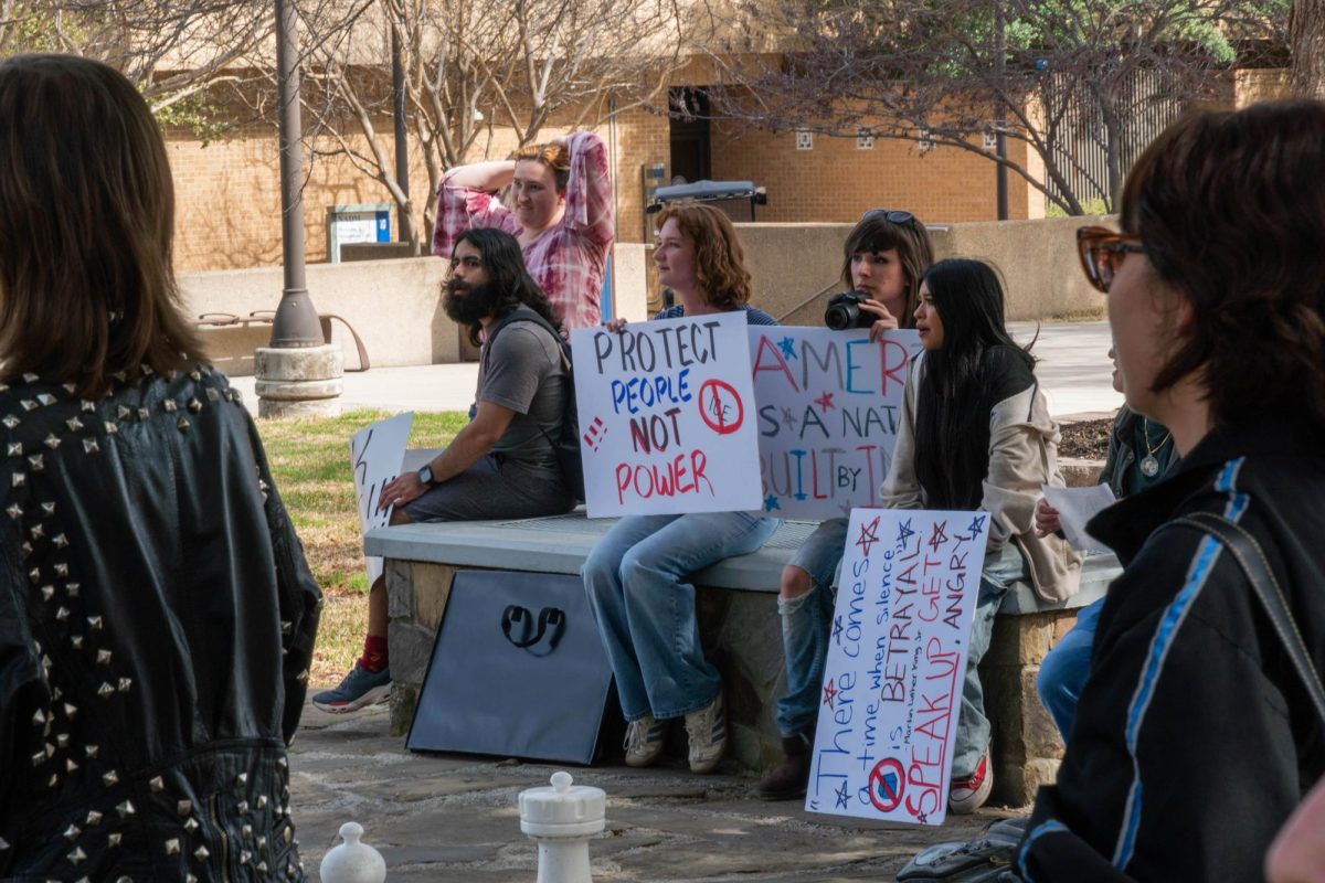 ICE walkout members sitting on half wall with signs and cameras.